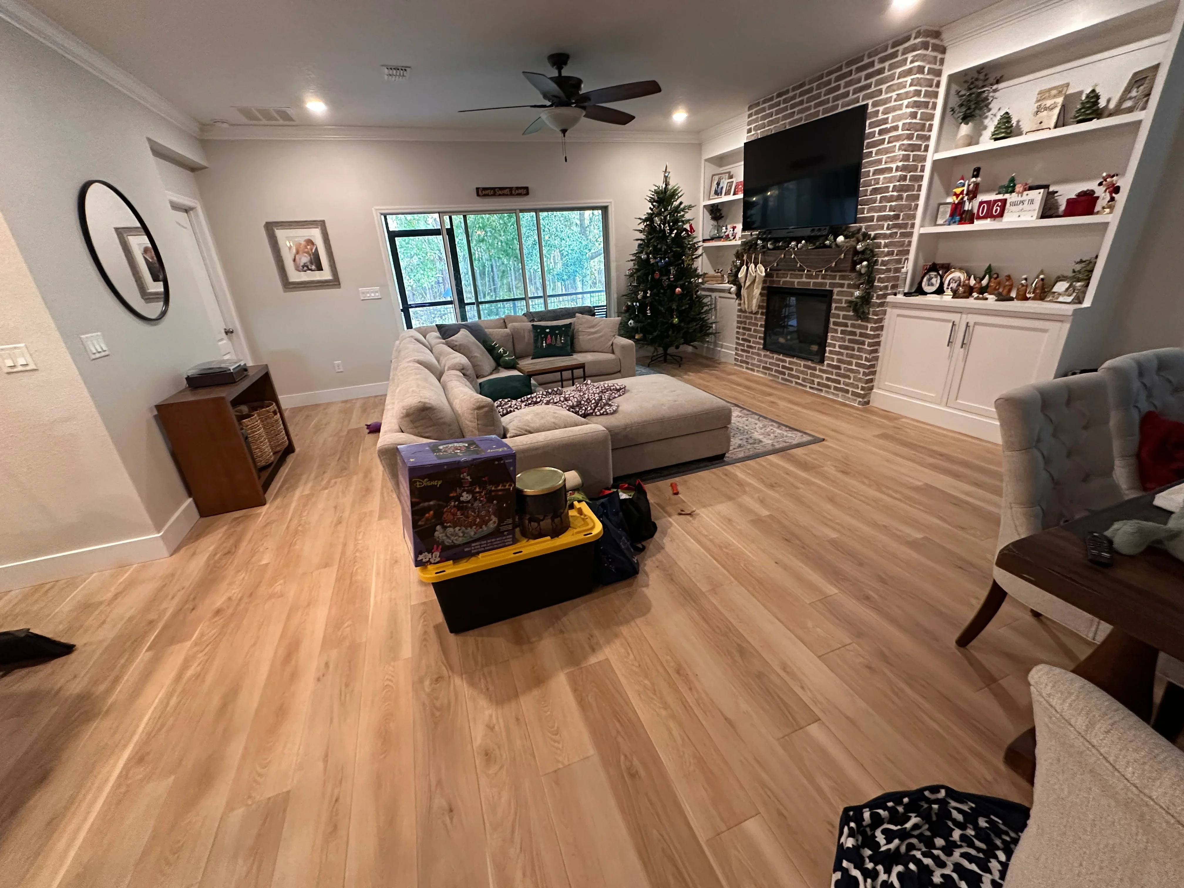 Luxury vinyl plank flooring installed in living room with brick fireplace and built-in shelving