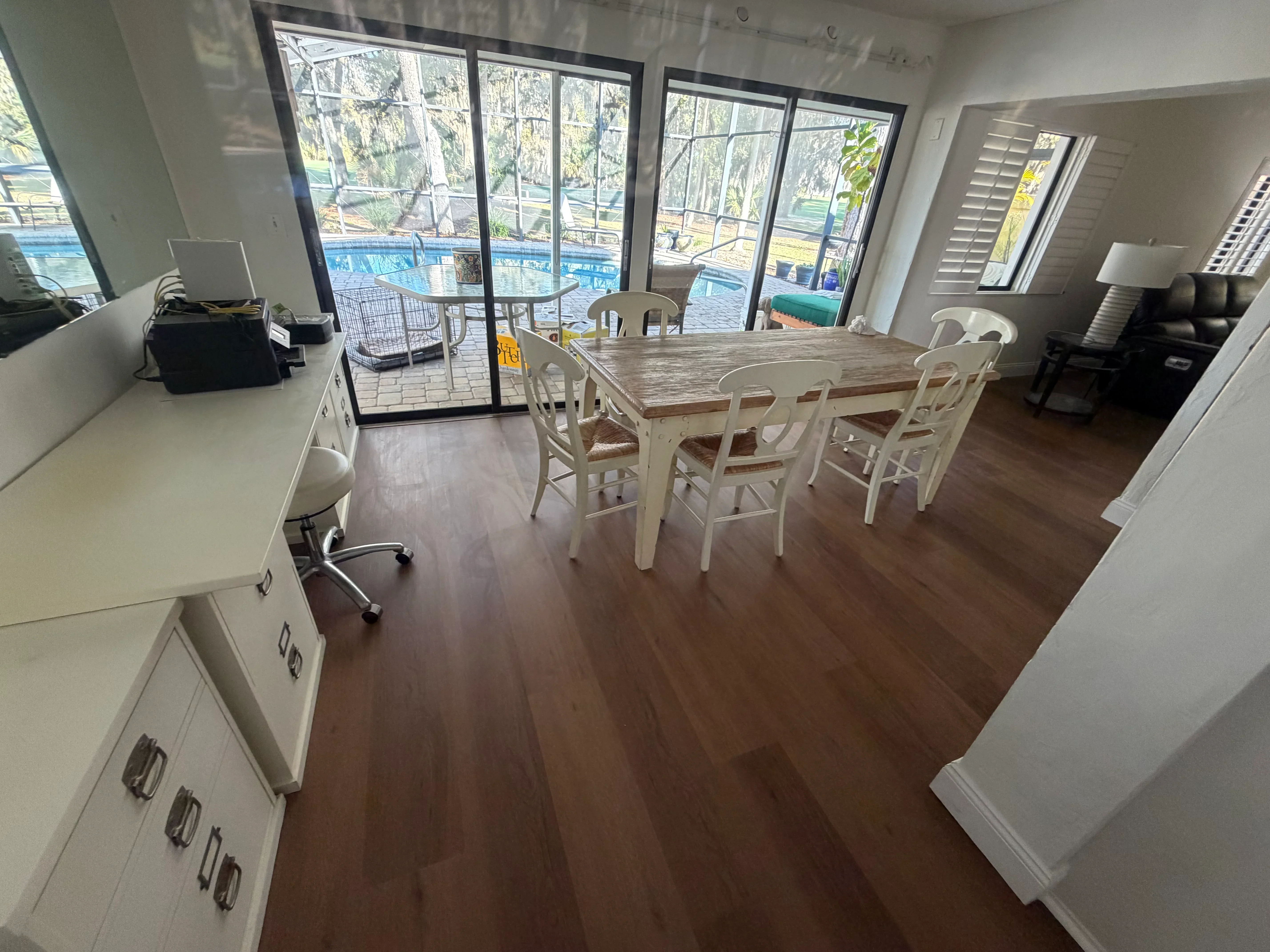 Dark wood-look vinyl plank flooring in open living space with dining table and pool view doors