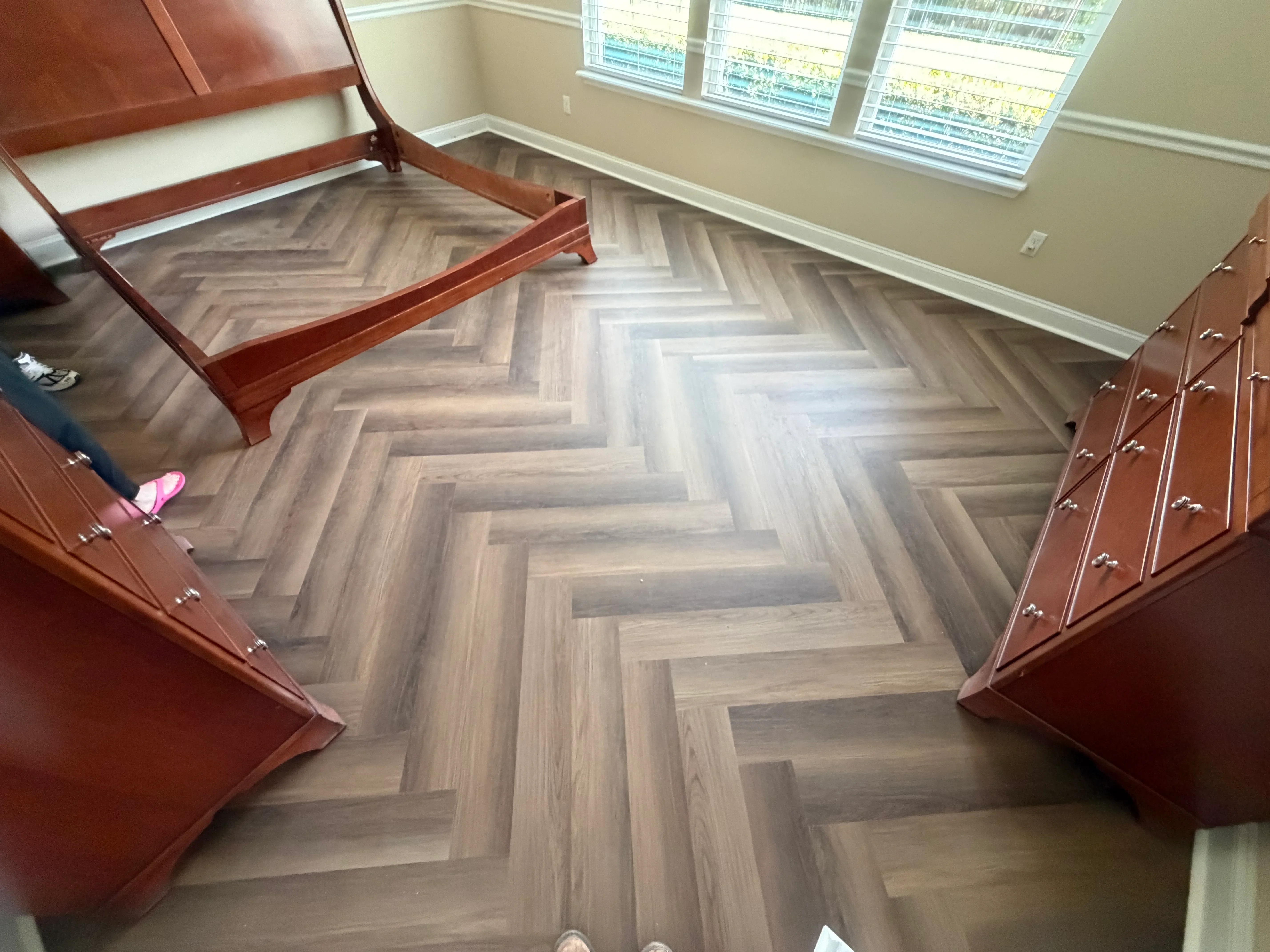 Herringbone pattern wood flooring in gray and tan tones installed in bedroom with wood furniture