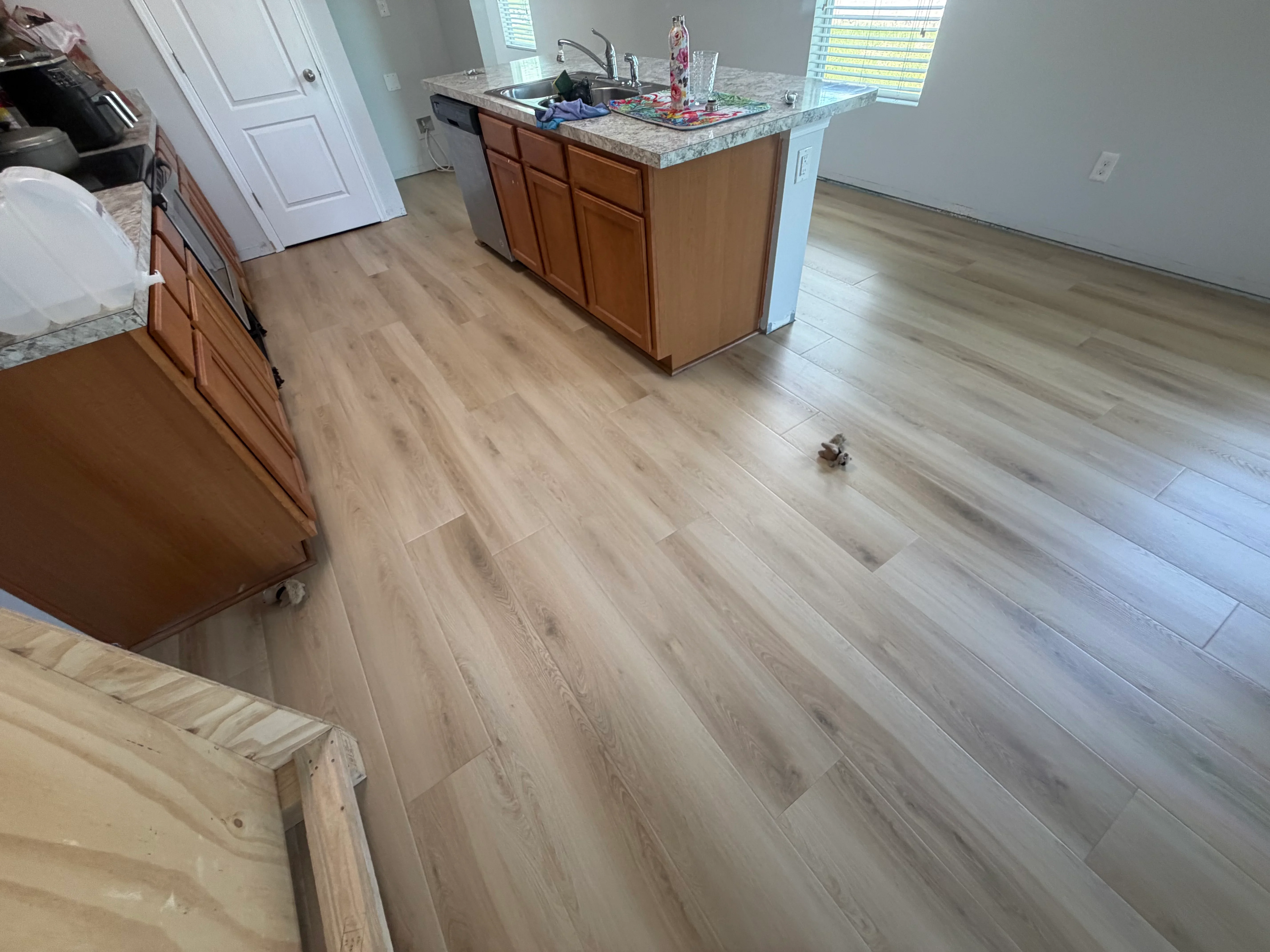 Light gray luxury vinyl plank flooring installed in kitchen with wood cabinetry and granite countertops