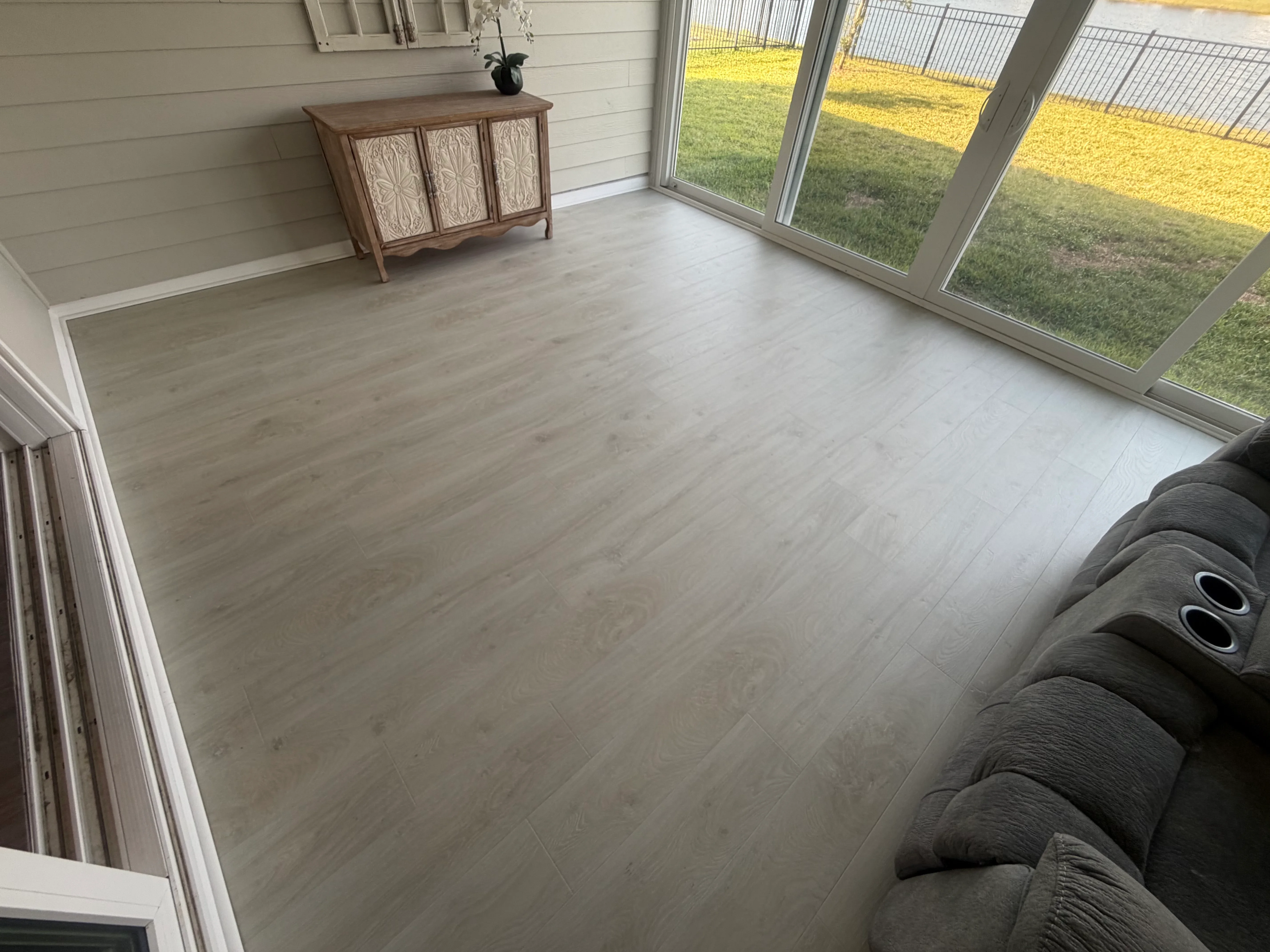 Light gray luxury vinyl plank flooring installed in sunroom with glass doors and white trim