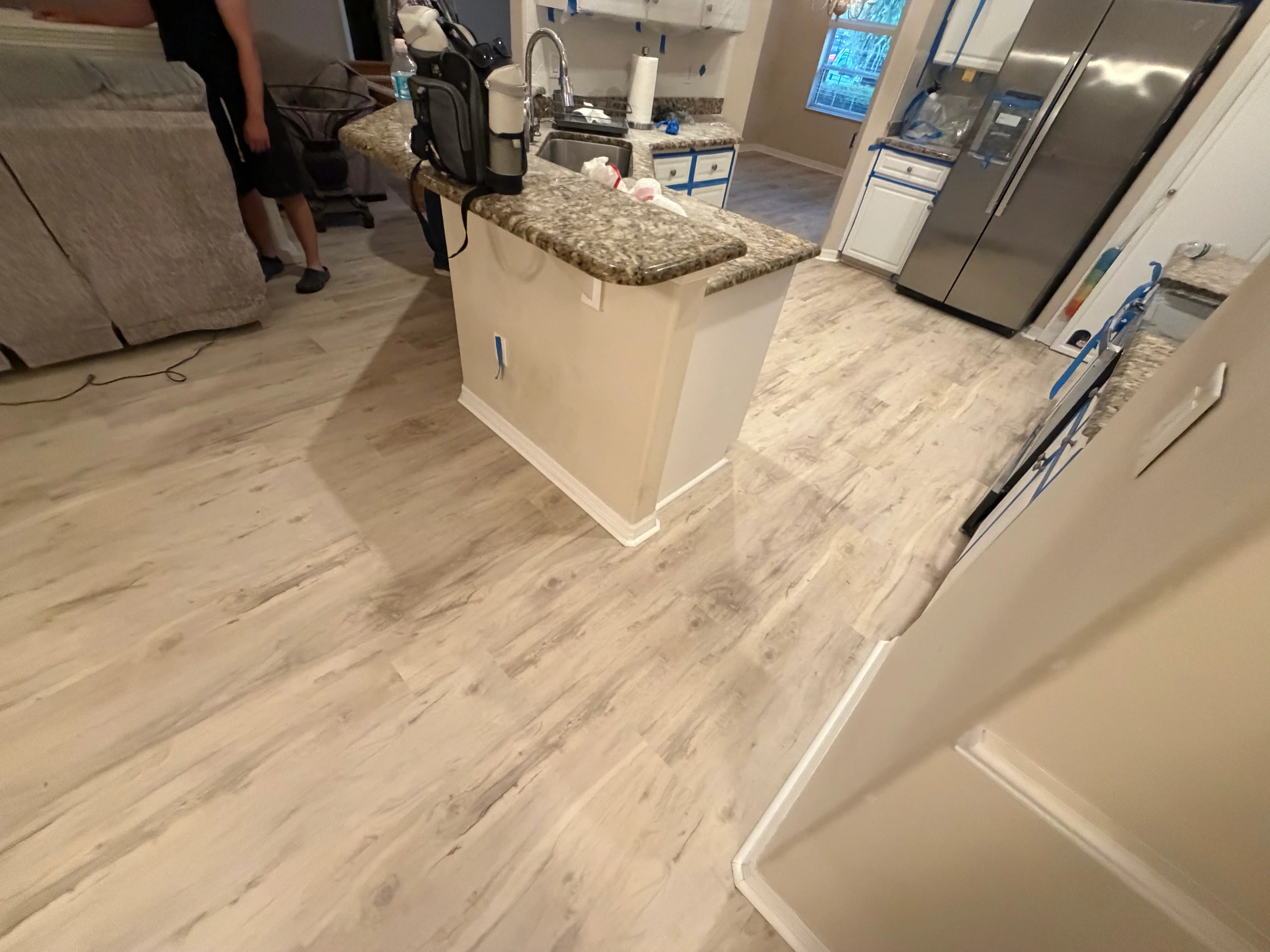 Light wood-look vinyl plank flooring installed in kitchen with island and granite countertop