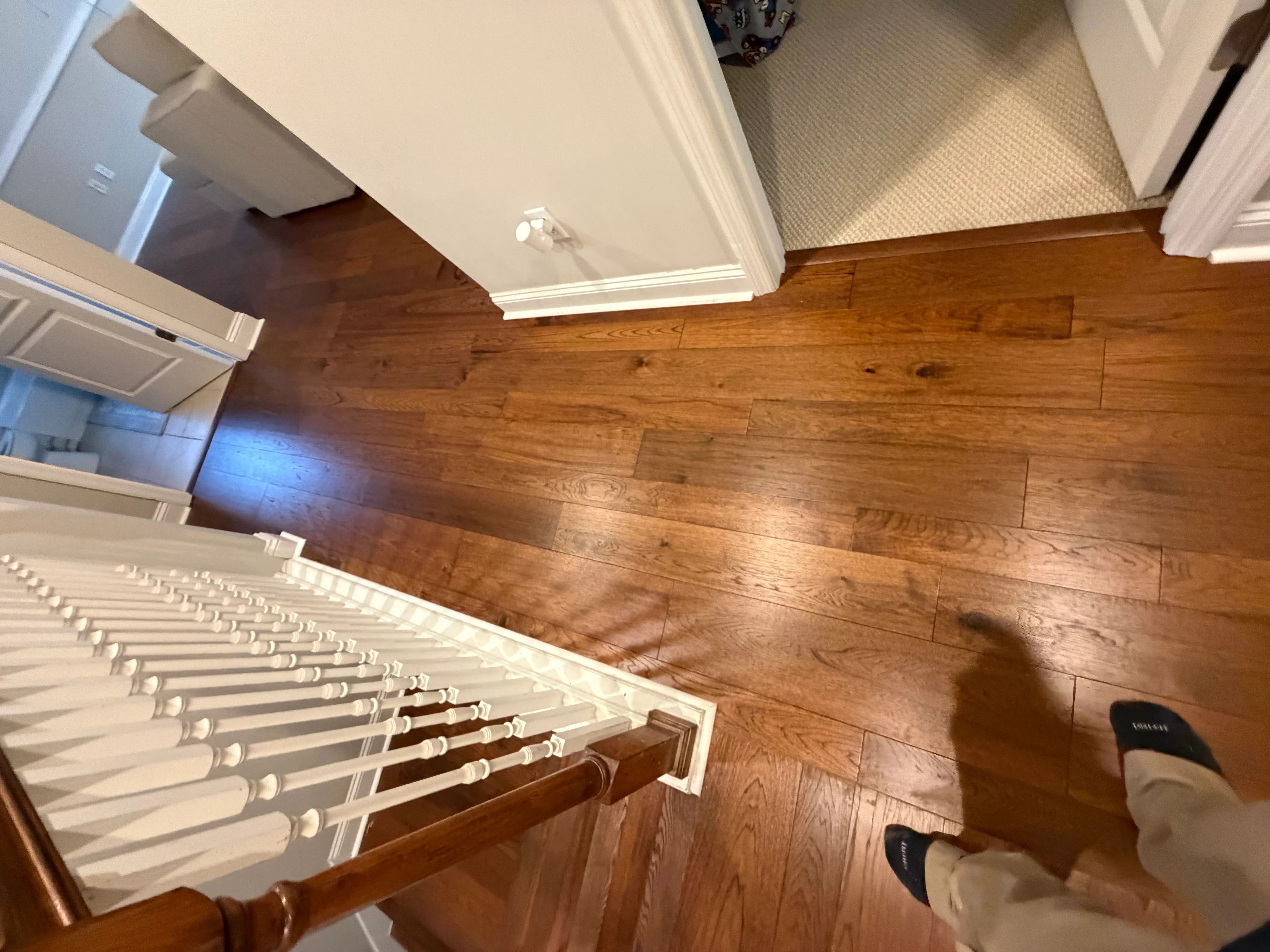 Hardwood floor installation with white trim and spindle stair railing in entryway