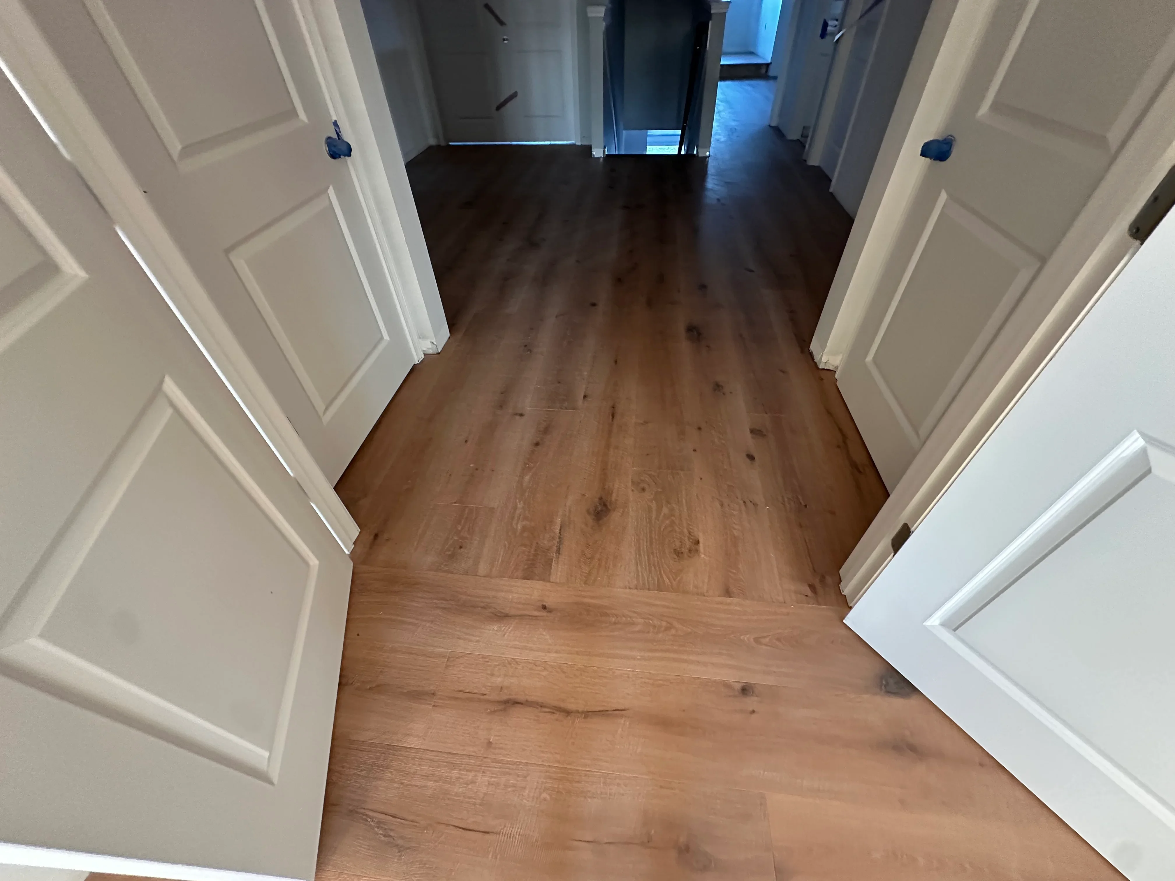 Hallway with installed laminate wood flooring, white trim, and six-panel doors
