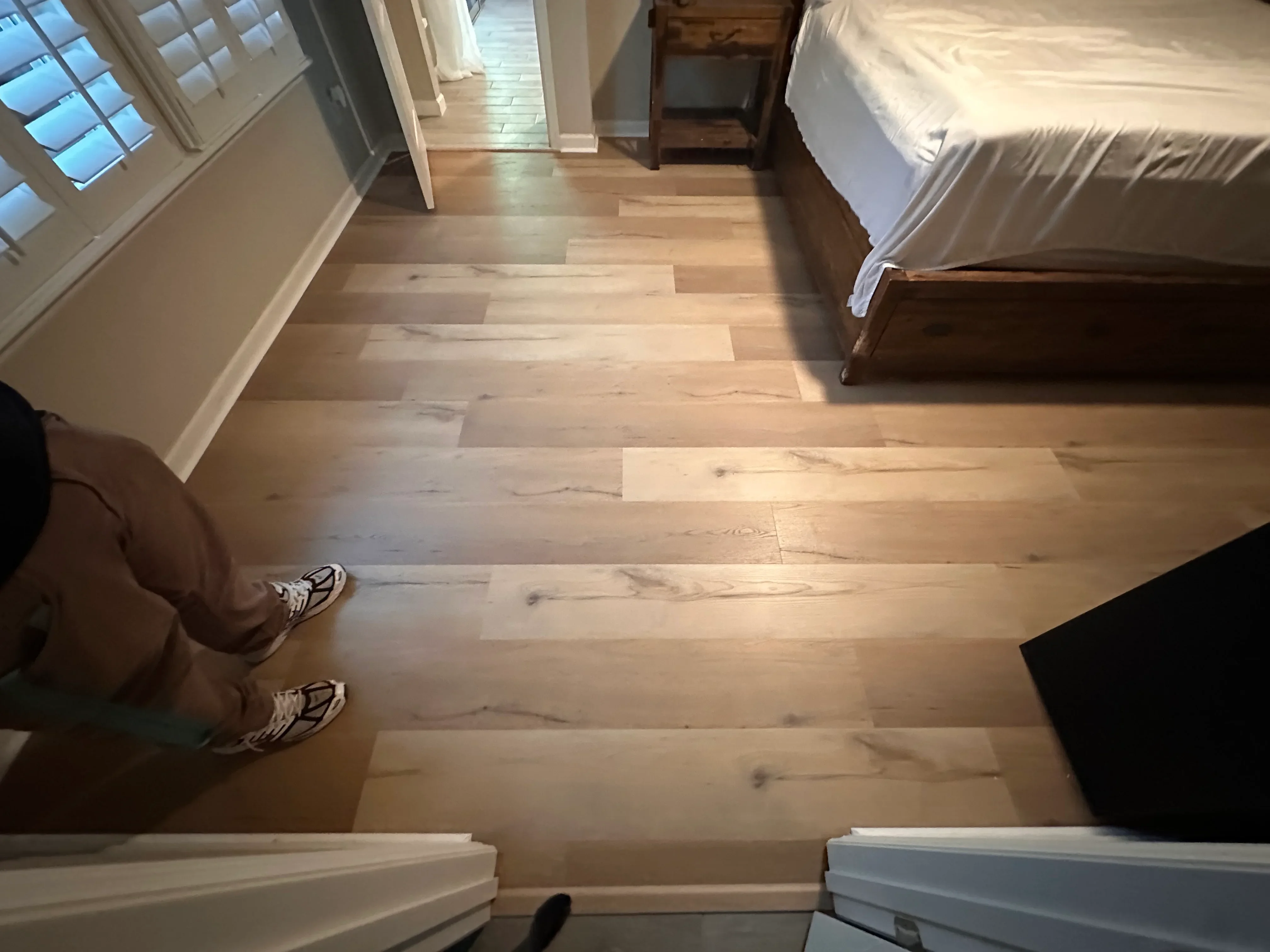 Light oak hardwood flooring with plank layout in bedroom with white trim and baseboards