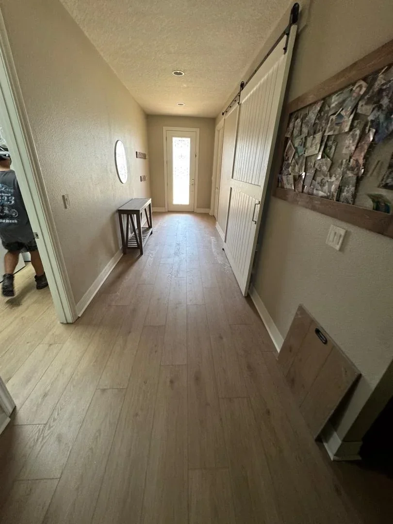 Wood-look laminate flooring installation in hallway with white trim and recessed lighting