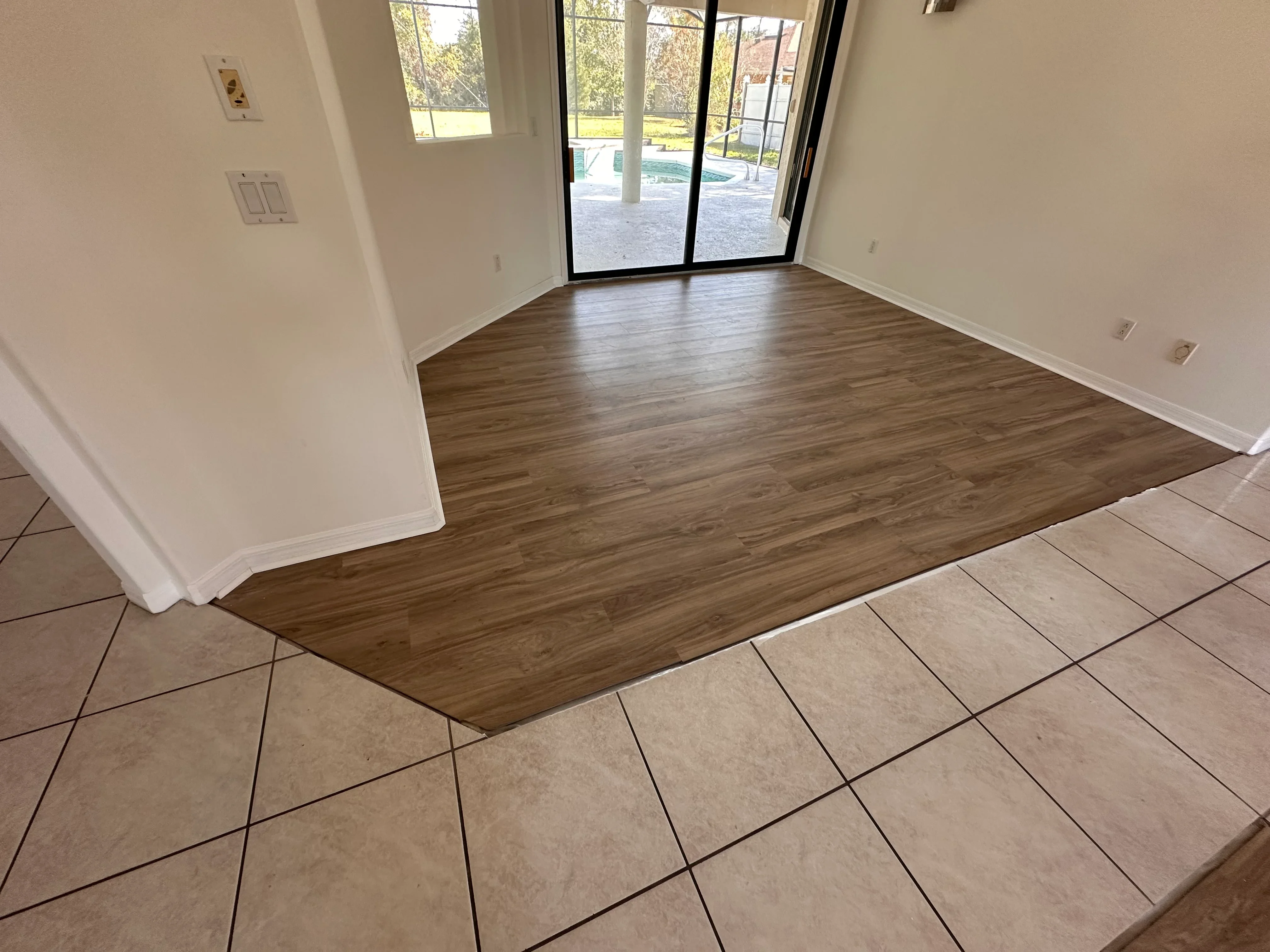 Luxury vinyl plank flooring installed in room with ceramic tile transition and glass doors