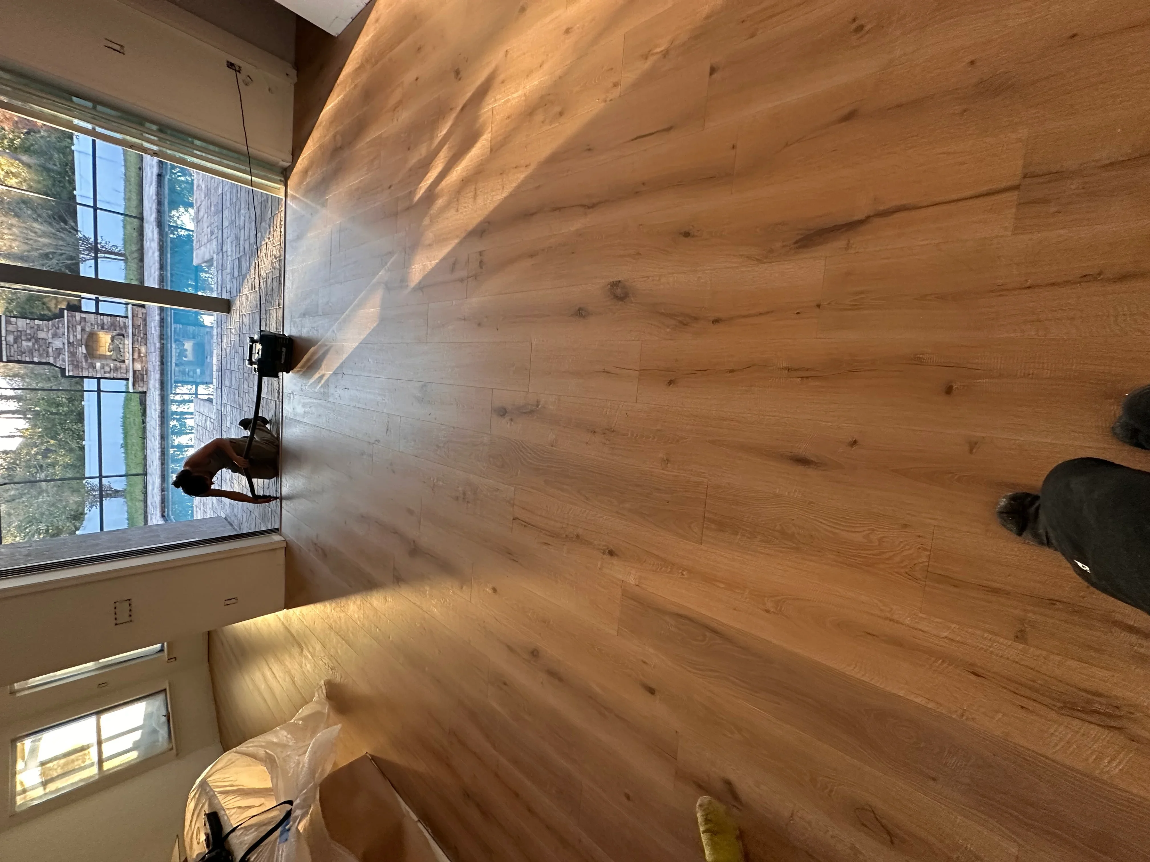 Wide plank hardwood flooring installation in room with vaulted ceiling and windows