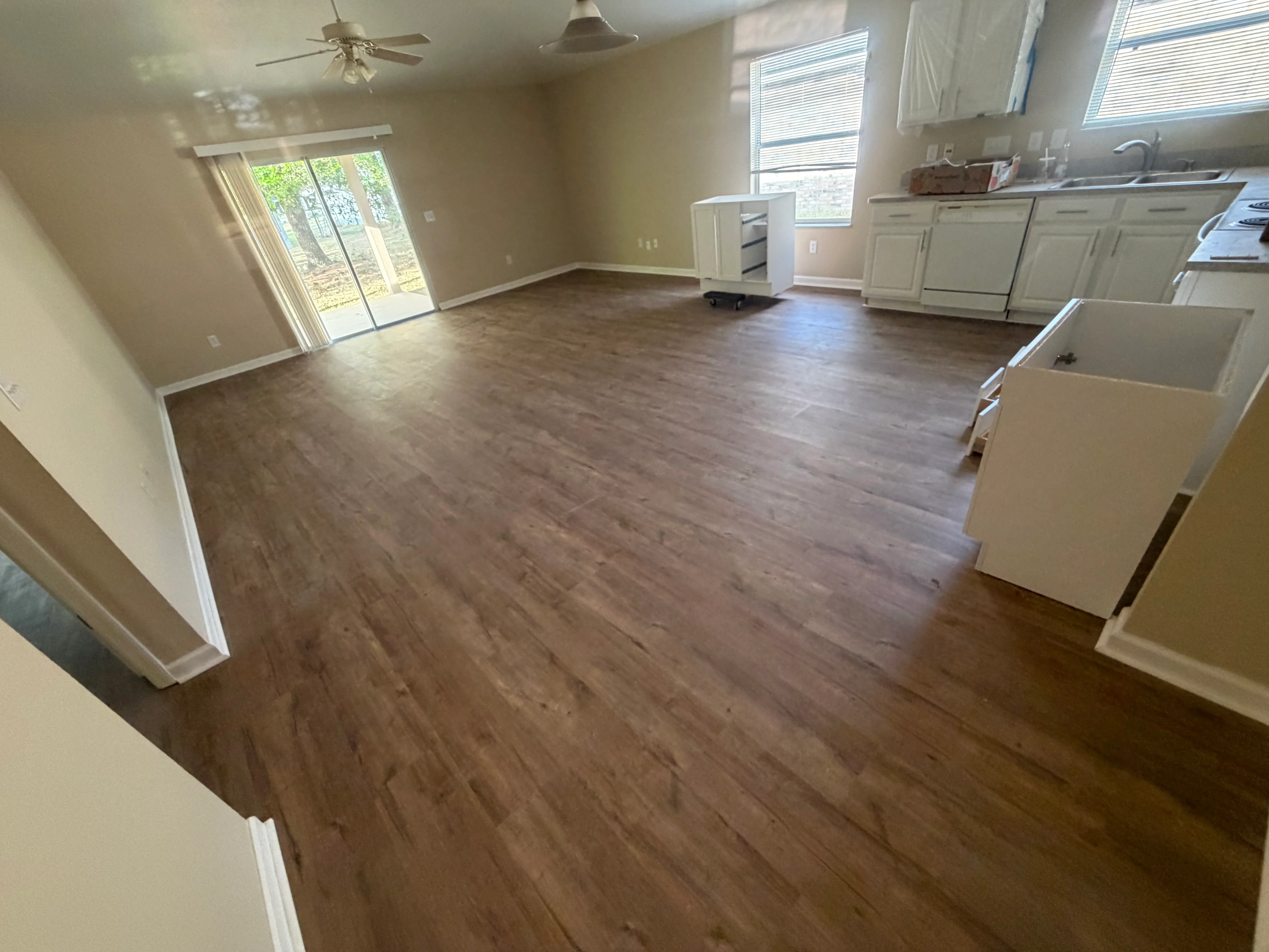 Wood-grain laminate flooring installed in kitchen and living room with white trim