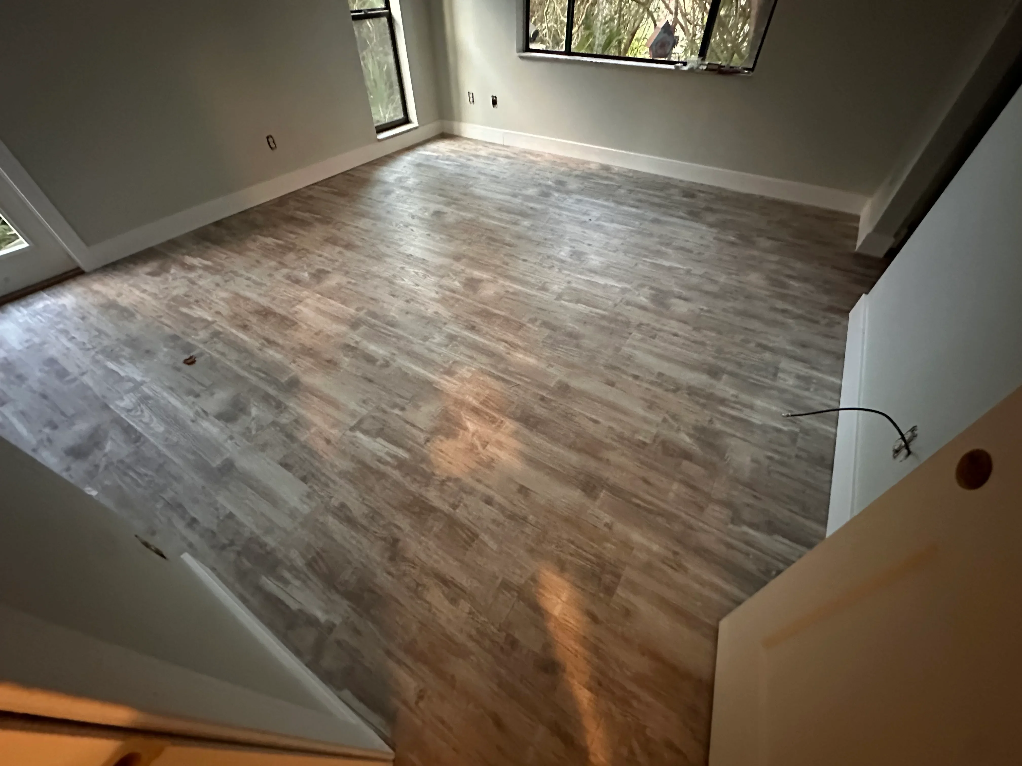Luxury vinyl plank flooring with gray wood-grain pattern installed in residential room with white trim
