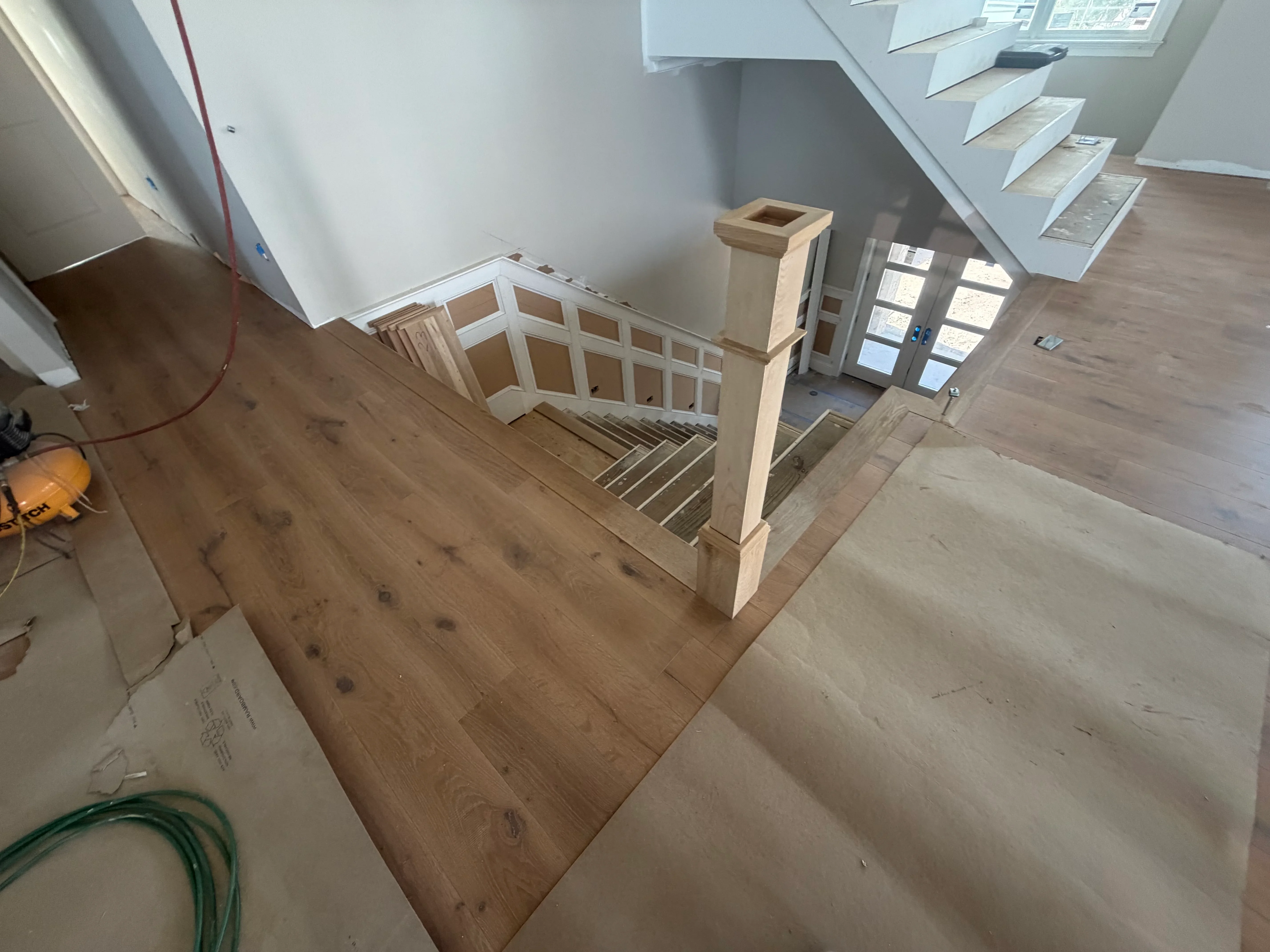Hardwood flooring installation with custom wood stair railing and white trim in multi-level space