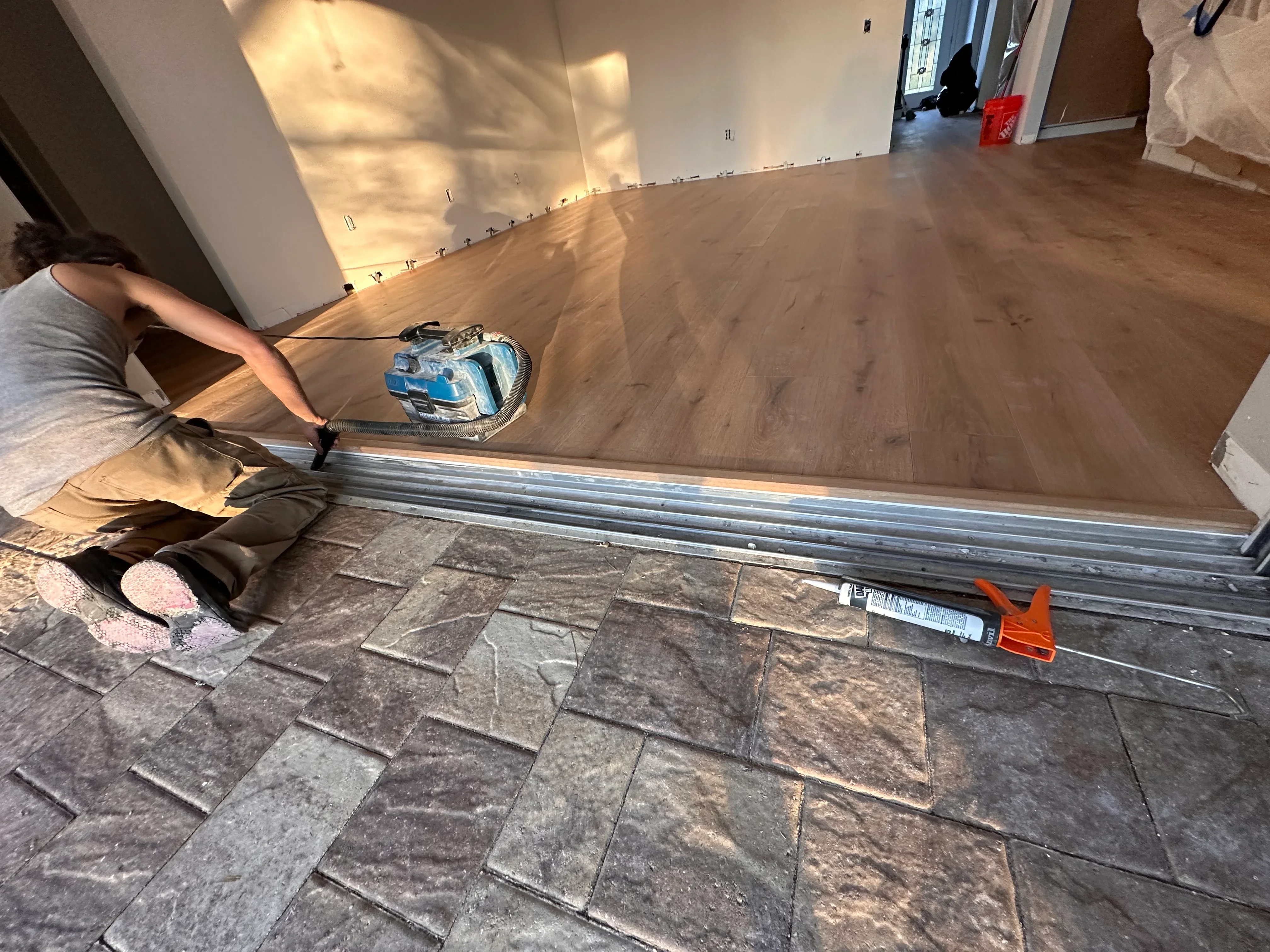 Worker installing luxury vinyl plank flooring with metal transition strip and professional equipment