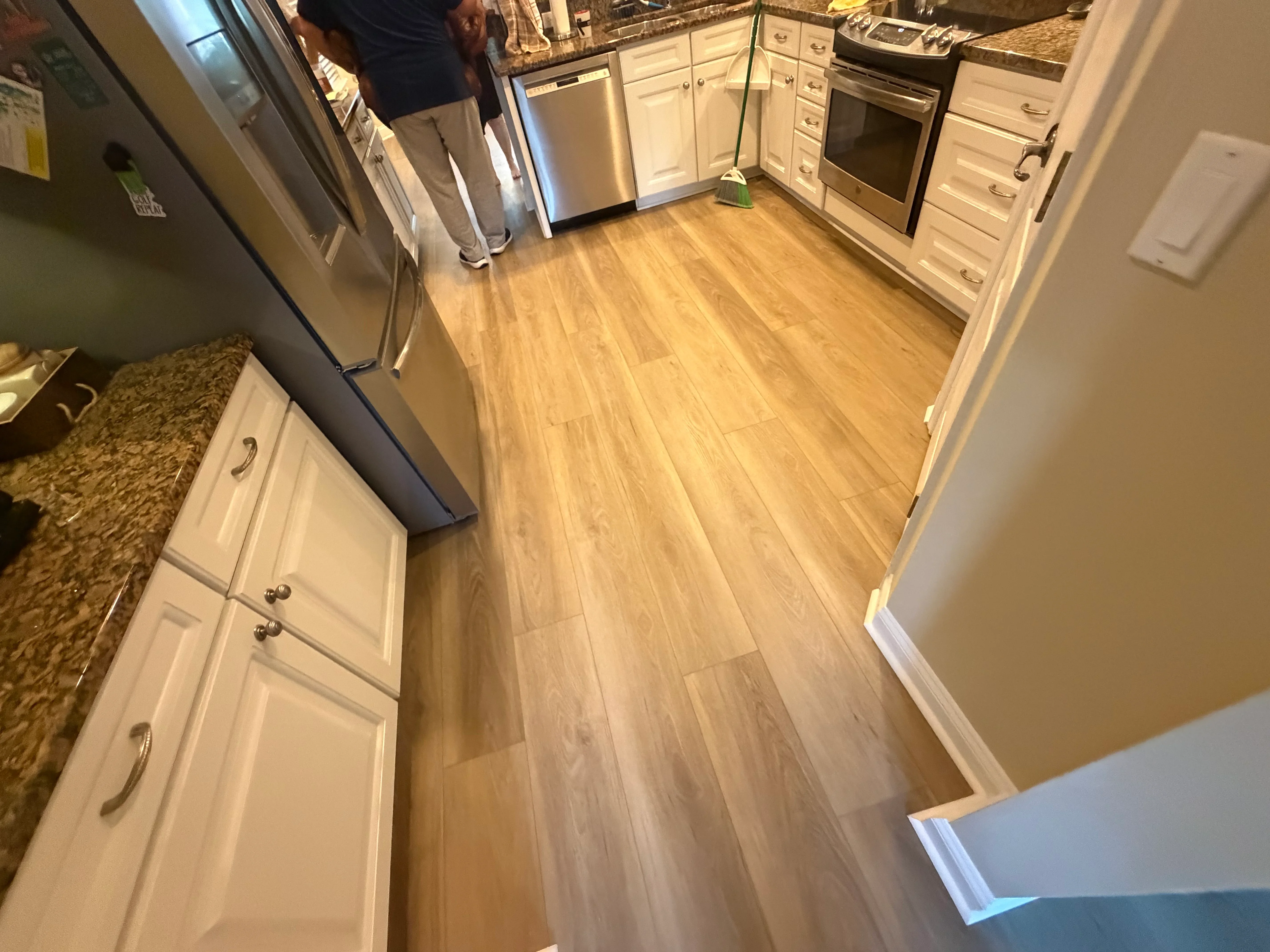 Wood-tone laminate flooring installed in kitchen with white cabinets and stainless steel appliances