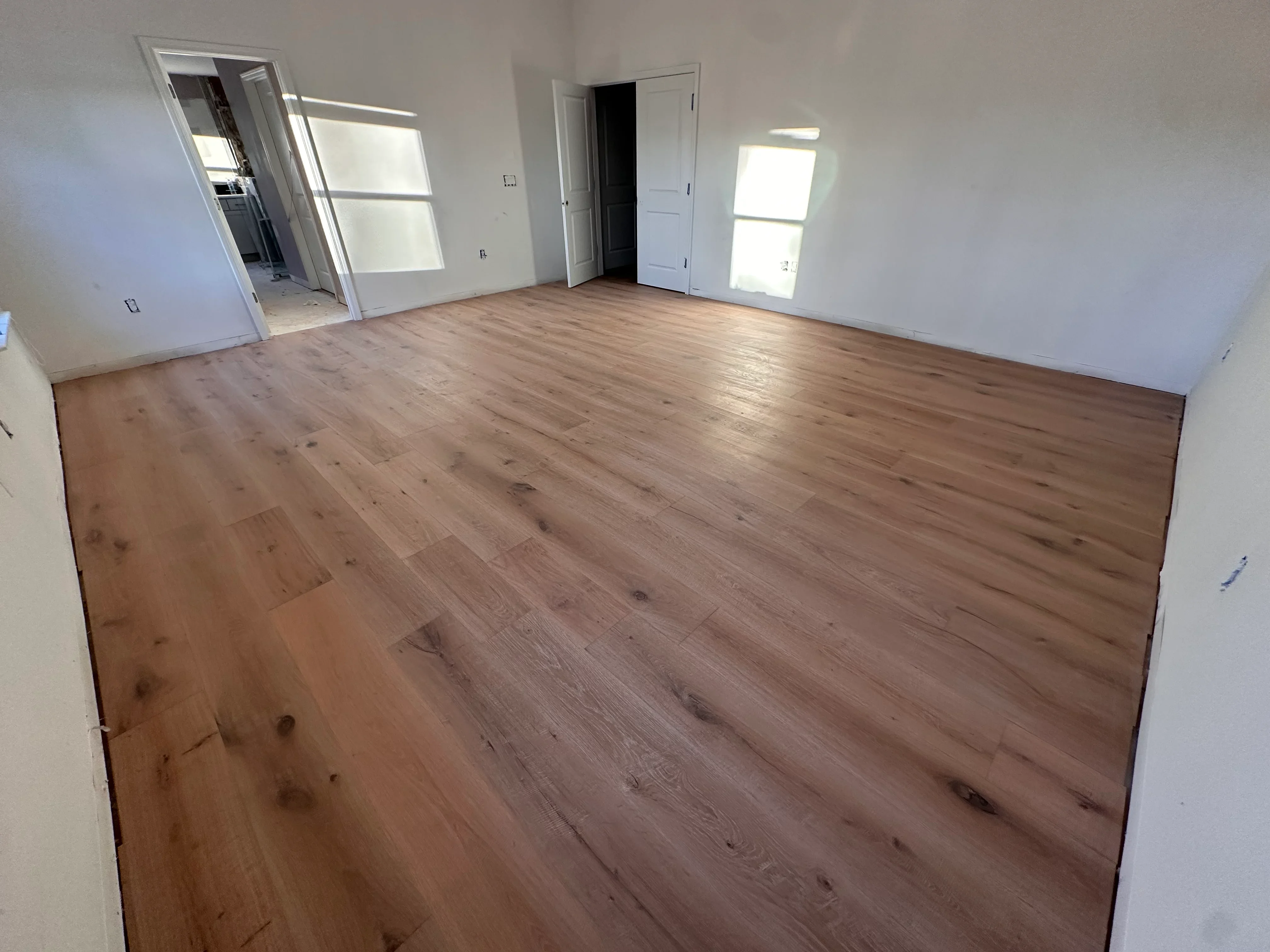 Newly installed medium-brown hardwood flooring with plank pattern in open room with white walls and doors