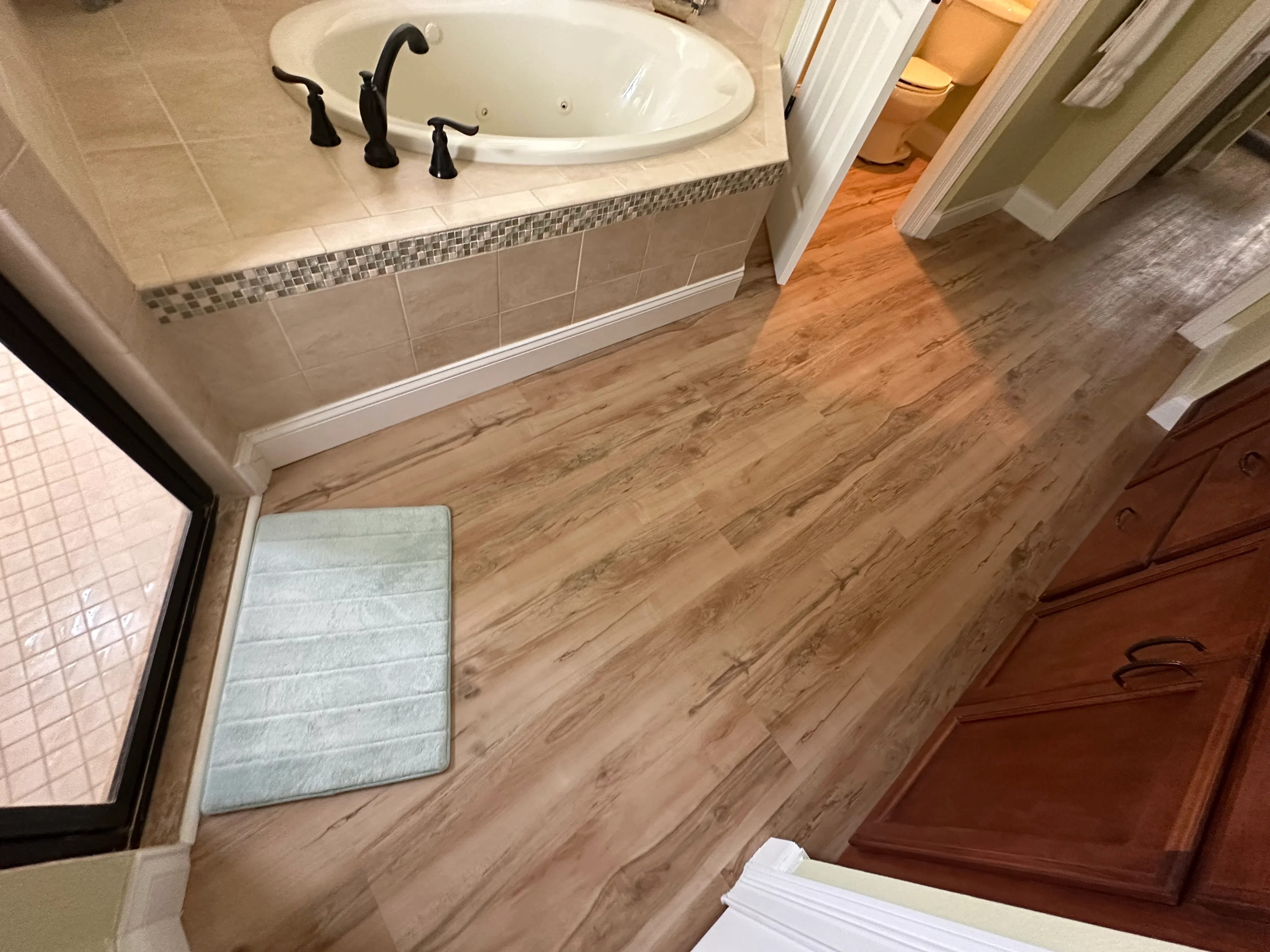 Luxury vinyl plank flooring installed in master bathroom with soaking tub and decorative tile accent